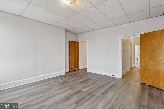 spare room with a drop ceiling, wood finished floors, and baseboards