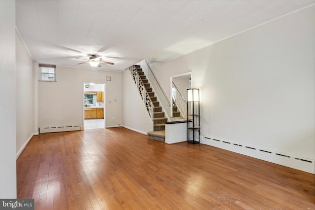 unfurnished living room with baseboard heating, a ceiling fan, wood-type flooring, and stairs