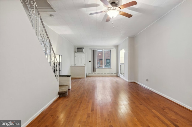 unfurnished living room with baseboard heating, stairs, wood-type flooring, baseboards, and ceiling fan