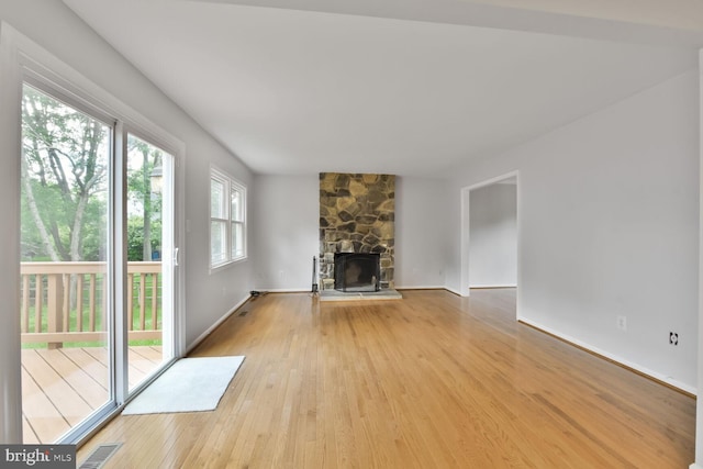 unfurnished living room with wood finished floors, a stone fireplace, and baseboards