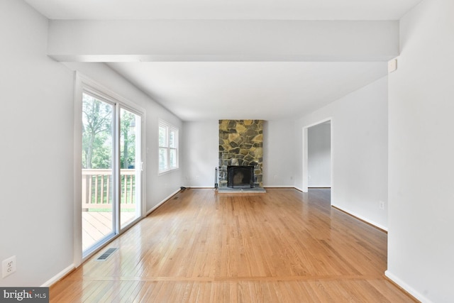 unfurnished living room with light wood-style flooring, a stone fireplace, and baseboards