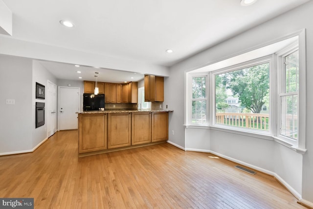 kitchen with black appliances, brown cabinets, light wood-style floors, baseboards, and a peninsula