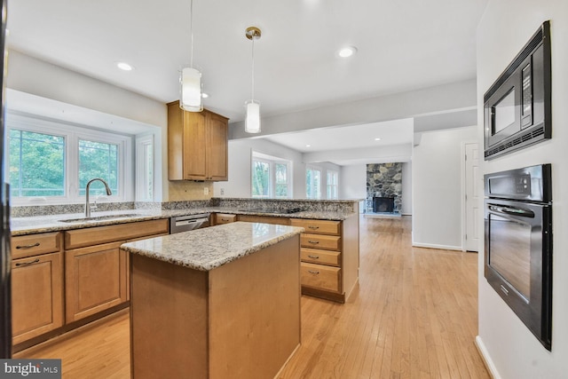 kitchen with black appliances, a sink, a peninsula, a kitchen island, and light stone counters