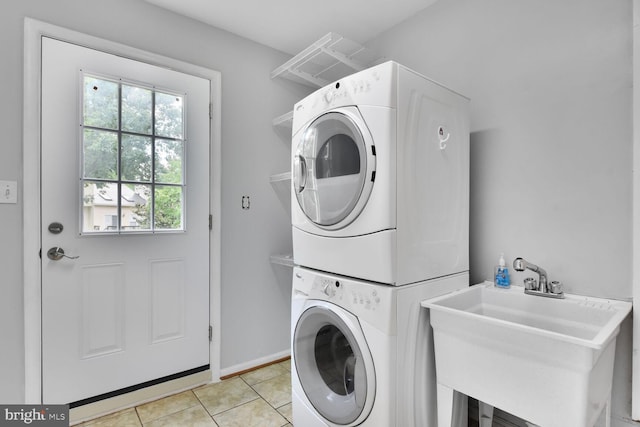 clothes washing area with stacked washer / drying machine, light tile patterned floors, and baseboards