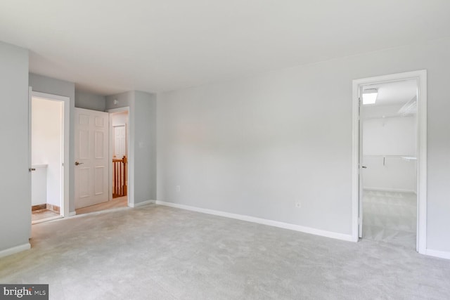 unfurnished bedroom with light colored carpet, baseboards, a walk in closet, and a closet