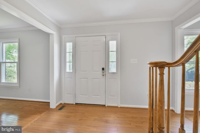 entrance foyer with light wood-style floors, healthy amount of natural light, baseboards, and crown molding