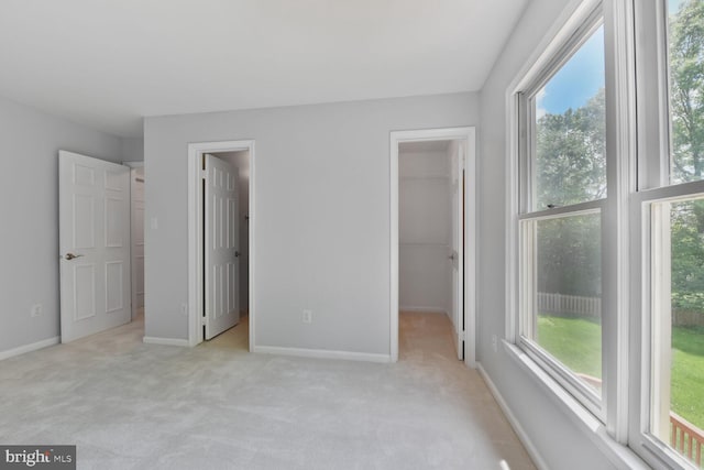 unfurnished bedroom with a walk in closet, multiple windows, and light carpet