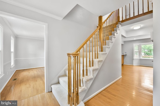 stairs with wood finished floors, ornamental molding, and baseboards
