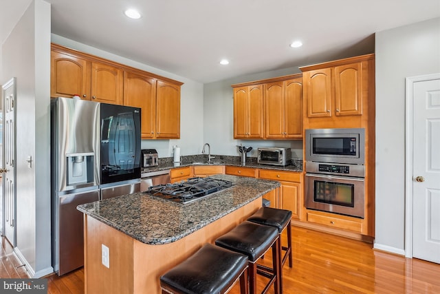 kitchen featuring stainless steel appliances, light wood-type flooring, a center island, dark stone countertops, and recessed lighting