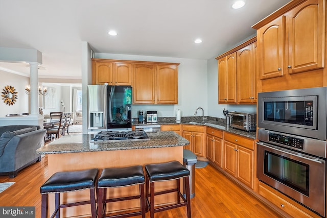 kitchen featuring appliances with stainless steel finishes, a kitchen breakfast bar, light wood-style floors, dark stone counters, and a kitchen island