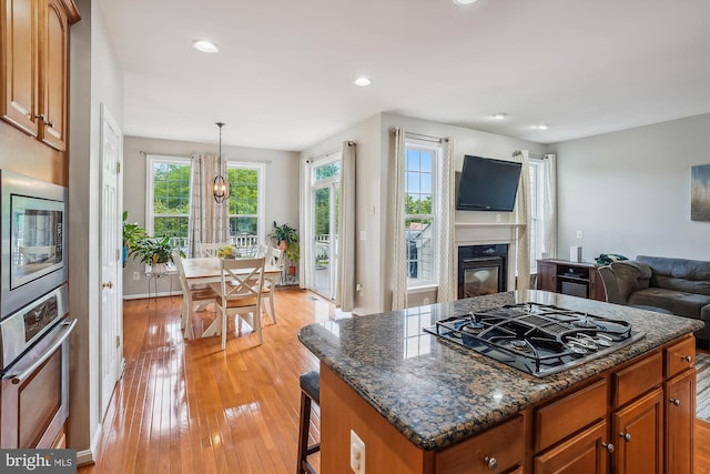 kitchen with appliances with stainless steel finishes, open floor plan, light wood-style flooring, brown cabinets, and recessed lighting