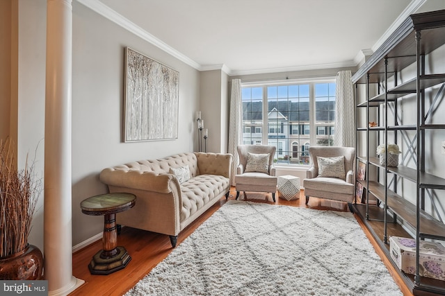 living area featuring wood finished floors, decorative columns, crown molding, and baseboards