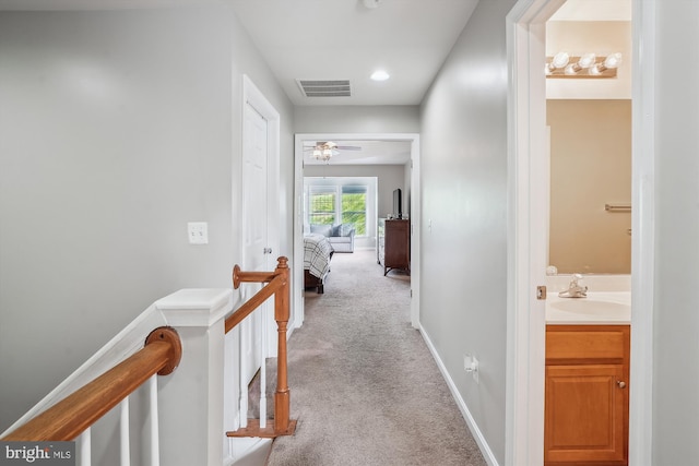 hall with carpet flooring, an upstairs landing, baseboards, and a sink