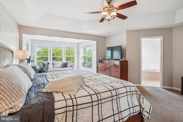 carpeted bedroom featuring a tray ceiling, baseboards, ceiling fan, and ensuite bath