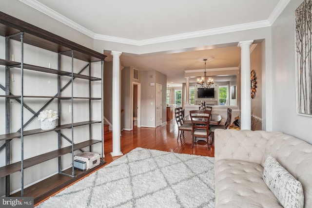 living room with decorative columns, wood finished floors, a chandelier, crown molding, and baseboards