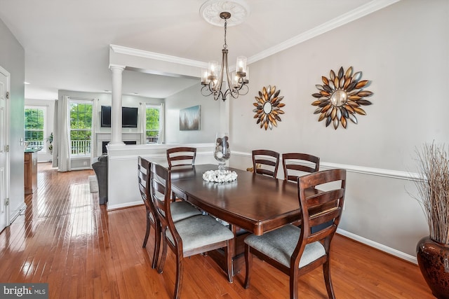 dining area featuring hardwood / wood-style flooring, decorative columns, a chandelier, crown molding, and baseboards