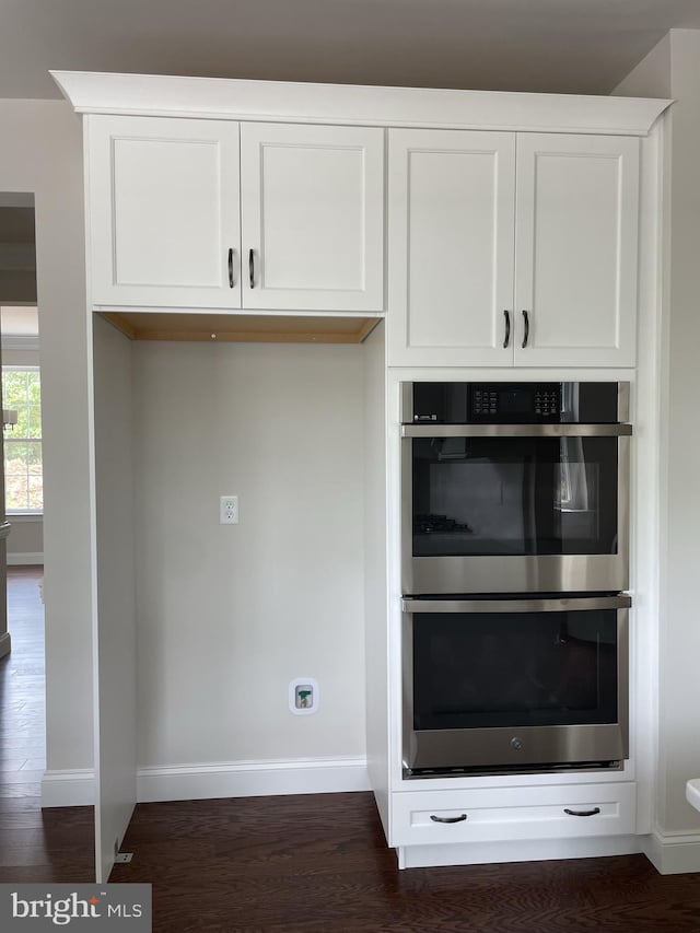 kitchen with double oven, baseboards, dark wood-type flooring, and white cabinetry