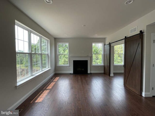 unfurnished living room featuring baseboards, dark wood-style floors, a fireplace with flush hearth, a barn door, and recessed lighting