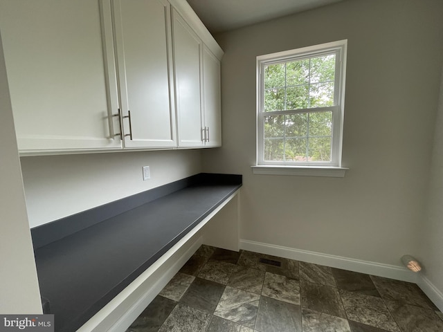 clothes washing area featuring baseboards and dark stone finish floors