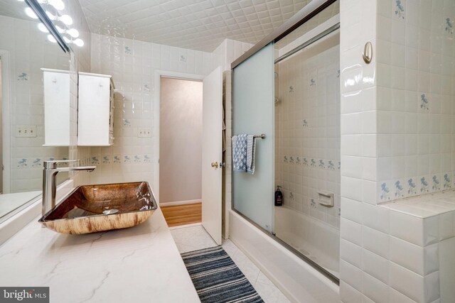 5101 Ampthill Dr, Alexandria, VA 22312 - bathroom with bath / shower combo with glass door, tile patterned floors, a sink, and tile walls
