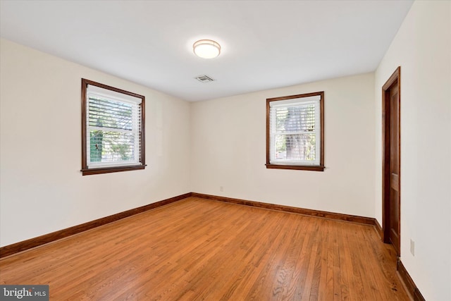 empty room featuring healthy amount of natural light, light wood-type flooring, and baseboards