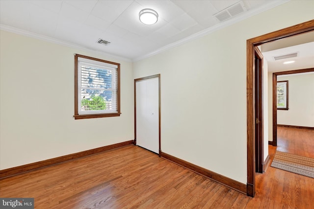 empty room featuring light wood-style floors, healthy amount of natural light, baseboards, and crown molding