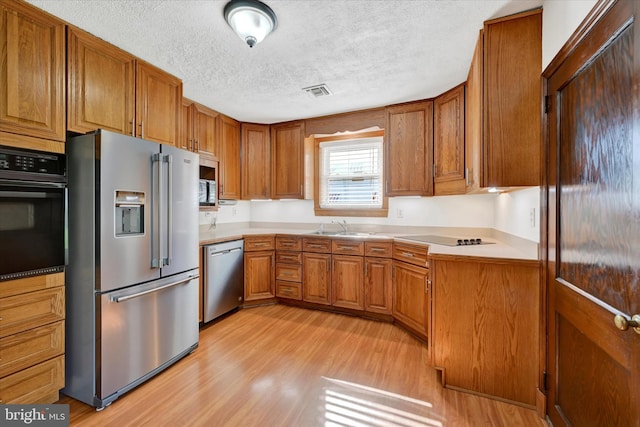 kitchen featuring black appliances, a textured ceiling, light wood finished floors, brown cabinetry, and a sink