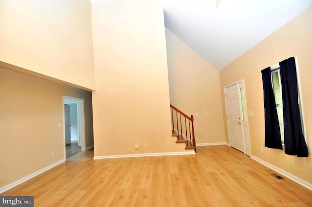 entrance foyer featuring high vaulted ceiling, stairway, light wood-style floors, and baseboards