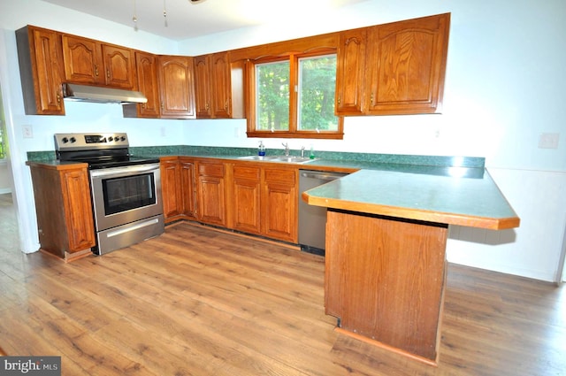 kitchen with appliances with stainless steel finishes, under cabinet range hood, a peninsula, a sink, and brown cabinets