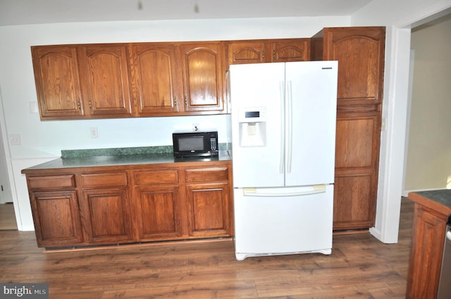 kitchen with white fridge with ice dispenser, black microwave, brown cabinetry, dark countertops, and dark wood-style floors