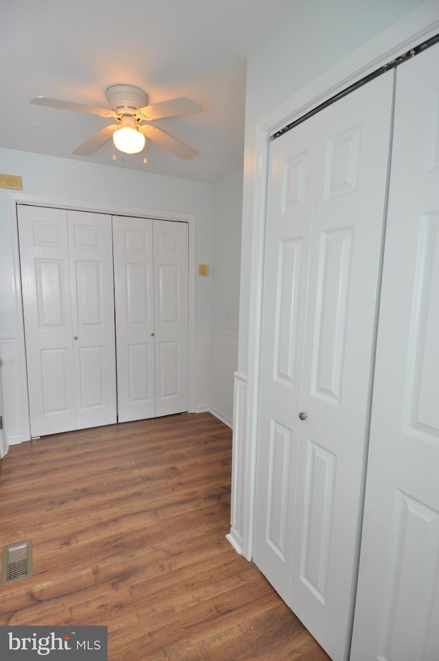 unfurnished bedroom featuring wood finished floors, multiple closets, and a ceiling fan
