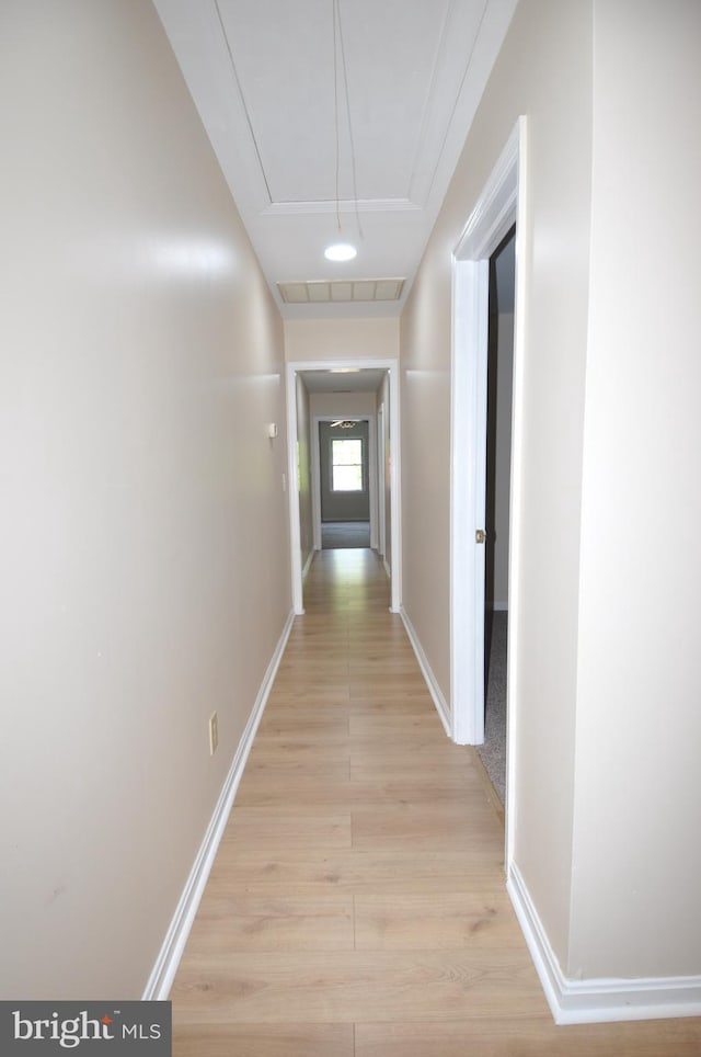 corridor with attic access, light wood-style flooring, and baseboards