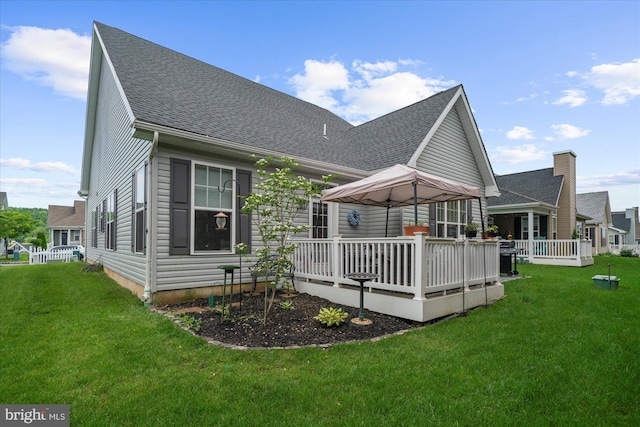 rear view of house featuring a wooden deck, a lawn, and roof with shingles