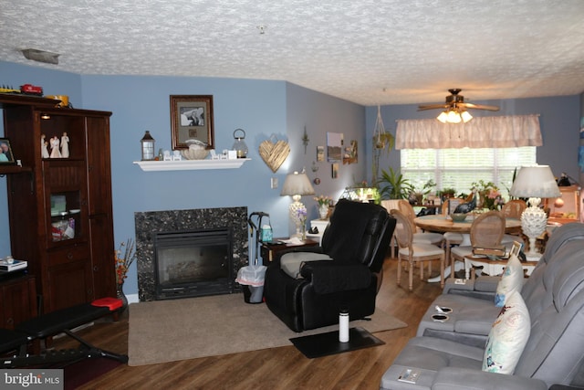 living area featuring wood finished floors, a tile fireplace, ceiling fan, and a textured ceiling
