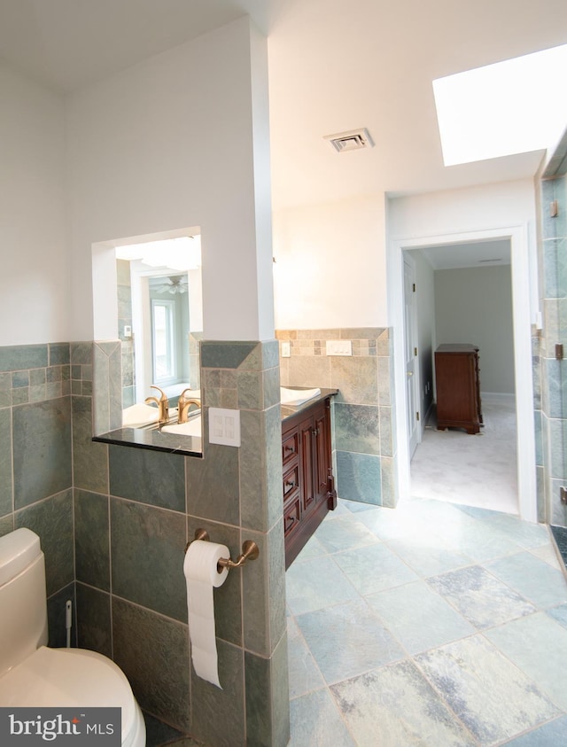 5470 Moose Lodge Rd, Cambridge, MD 21613 - bathroom with tile walls, vanity, a skylight, a wainscoted wall, and stone finish floors