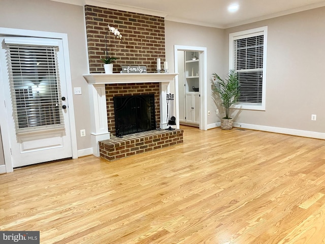 unfurnished living room with wood finished floors, a brick fireplace, crown molding, and baseboards
