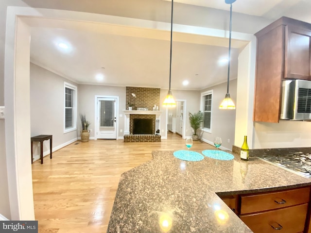 kitchen with stainless steel appliances, dark stone counters, light wood-style floors, a fireplace, and open floor plan