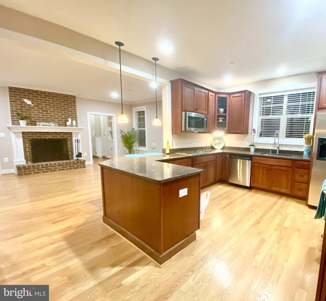 kitchen with stainless steel appliances, a sink, light wood finished floors, a peninsula, and open floor plan