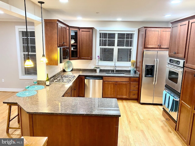 kitchen featuring appliances with stainless steel finishes, a sink, light wood finished floors, a peninsula, and recessed lighting