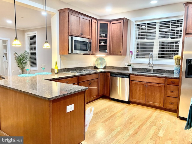 kitchen featuring stainless steel appliances, a sink, light wood-style flooring, dark stone counters, and a peninsula