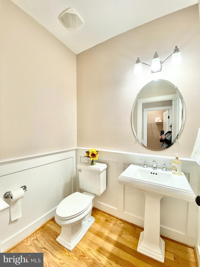 bathroom featuring toilet, wood finished floors, wainscoting, and a decorative wall