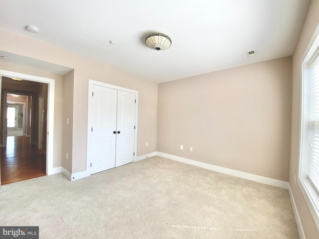 unfurnished bedroom featuring light colored carpet, baseboards, and a closet