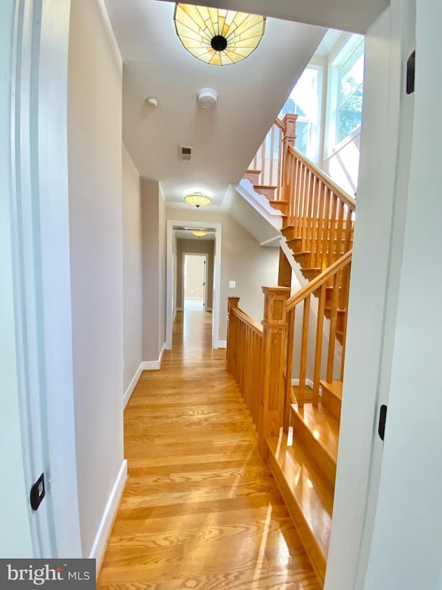 hall featuring light wood-style floors, baseboards, and stairs