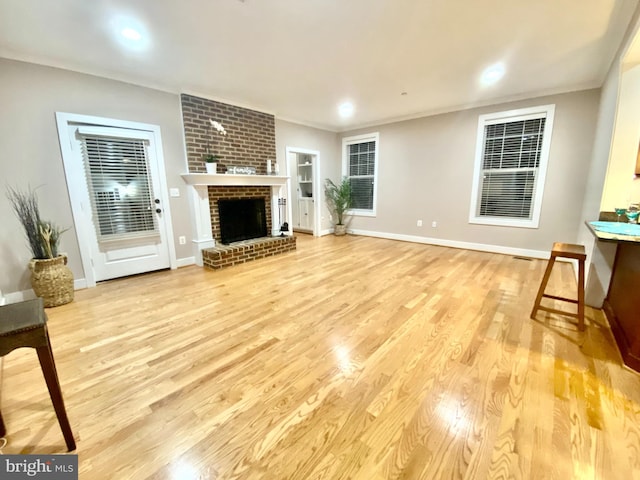unfurnished living room featuring light wood finished floors, a brick fireplace, baseboards, and crown molding