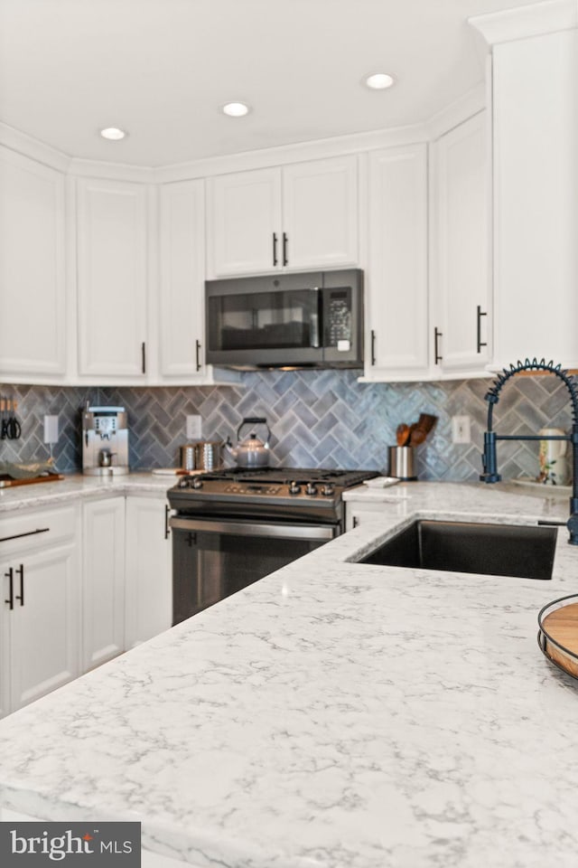 20387 Birchmere Ter, Ashburn, VA 20147 - kitchen featuring stainless steel gas stove, a sink, white cabinets, light stone countertops, and decorative backsplash
