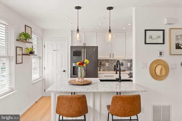 20387 Birchmere Ter, Ashburn, VA 20147 - kitchen featuring stainless steel refrigerator with ice dispenser, white cabinets, a kitchen bar, tasteful backsplash, and light wood finished floors