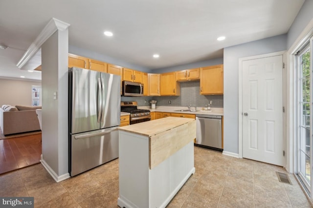 kitchen with stainless steel appliances, light brown cabinetry, a sink, decorative backsplash, and recessed lighting