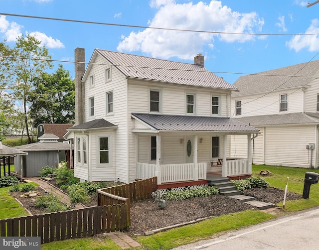 country-style home featuring a chimney, covered porch, metal roof, and fence