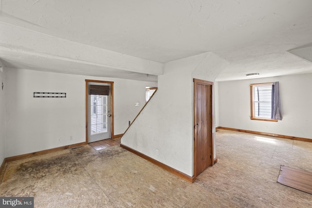 unfurnished room featuring baseboards, a textured ceiling, and stairway