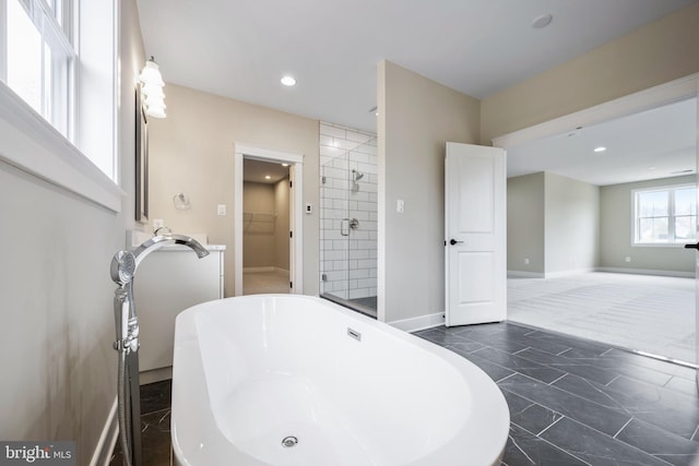 bathroom with a stall shower, a spacious closet, a freestanding bath, recessed lighting, and baseboards